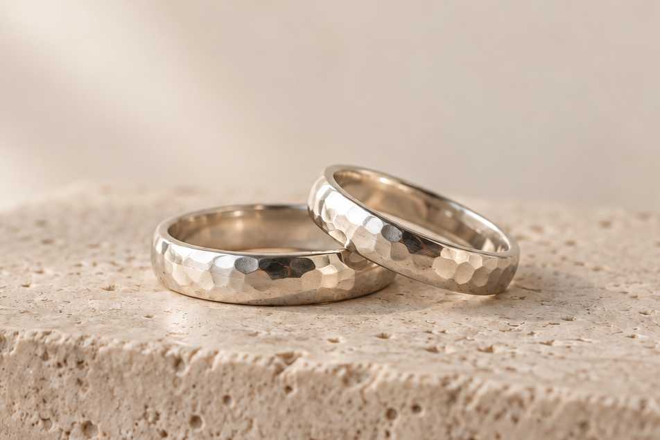 Two ring bands with hand-hammered faceted texture on a stone block.
