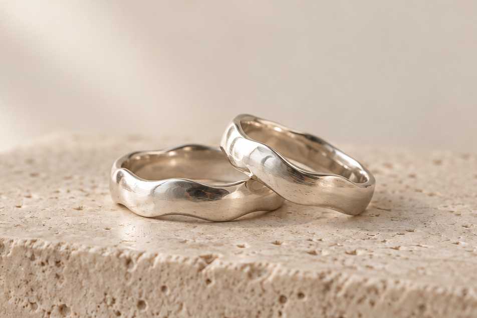 Two ring bands with gently wavy, organic edges on a stone block.